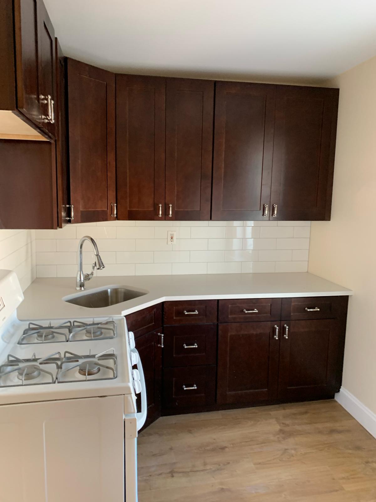 Clean and refurbished kitchen with dark brown cabinets and white tiles.